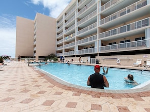 Un espace piscine doté de plusieurs niveaux de balcons, de chaises longues et d’une allée dallée.