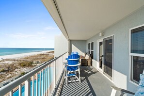 Een balkon met uitzicht op het strand, een blauwe stoel en een rieten stoel.