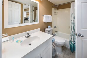 A bathroom with a white sink, toilet, and bathtub. There is a towel rack above the toilet and a shower curtain with a pattern. - Summerlin 103 - Shell Seekers Retreat (Fort Walton Beach)