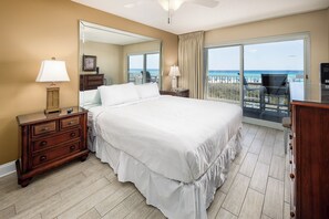 A bedroom with a large bed, a dresser, a mirror, and a balcony with a view of the beach. - Summerlin 103 - Shell Seekers Retreat (Fort Walton Beach)