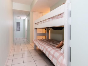 Un pasillo estrecho con una cama litera a la derecha, una puerta al final y una ventana pequeña a la izquierda.