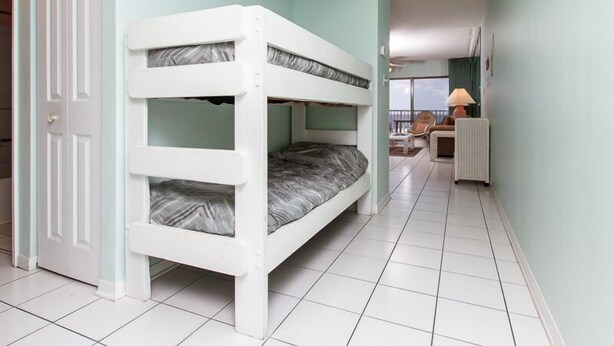 A bunk bed room with a door, a small table, and a lamp. - Emerald Towers West 2004 - Palms & Paradise (Fort Walton Beach)