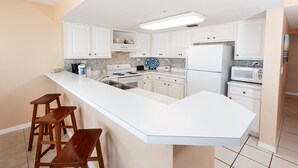 A modern kitchen with white cabinets, a large island with stools, a refrigerator, microwave, and a blender. - Islander 4002 - Whispering Waves (Fort Walton Beach)