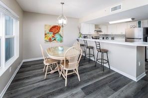A modern kitchen with white cabinets, a stainless steel refrigerator, and a dining area with a round table and chairs. - Islander 4002 - Whispering Waves (Fort Walton Beach)