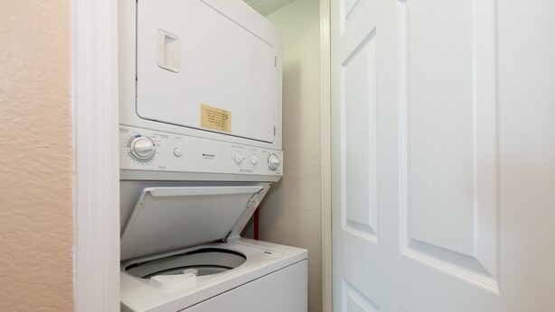 A compact laundry room with a front-loading washer and dryer, a control panel with various settings, and a door to the right. - Islander 4002 - Whispering Waves (Fort Walton Beach)