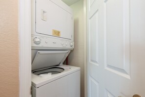 A compact laundry room with a front-loading washer and dryer, a control panel with various settings, and a door to the right. - Islander 4002 - Whispering Waves (Fort Walton Beach)