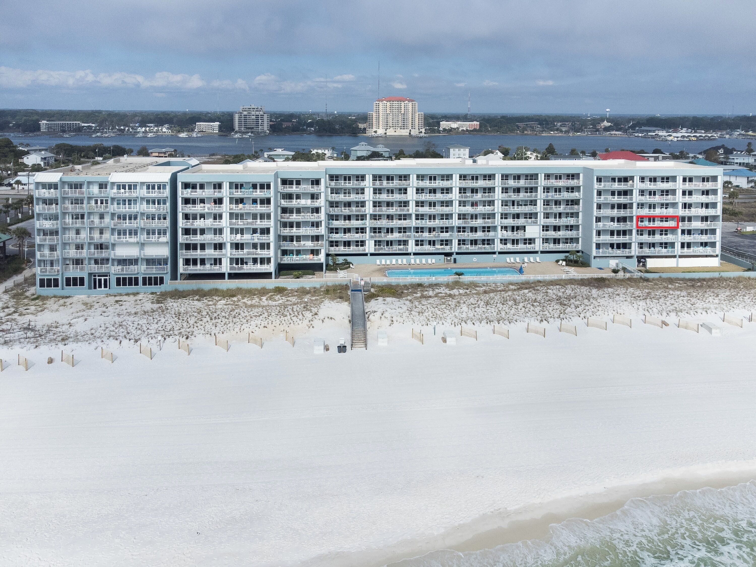 A beachfront hotel with multiple balconies, a swimming pool, and a beach in the foreground.