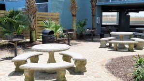 Un patio con mobiliario exterior, palmeras y fachada de un edificio azul.