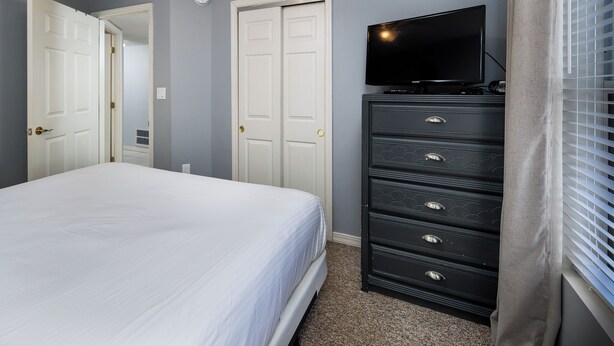 Un dormitorio con una cama, un aparador, un televisor y una puerta.