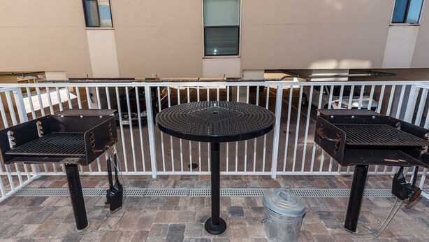 Eine Terrasse mit zwei Grillanlagen und einem runden Tisch, umgeben von einem weißen Zaun.