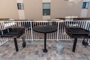 Eine Terrasse mit zwei Grillanlagen und einem runden Tisch, umgeben von einem weißen Zaun.