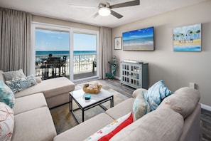A living room with a sofa, a coffee table, and a TV. There is a balcony with a view of the beach. - The Palms 203 - Endless Horizons (Fort Walton Beach)