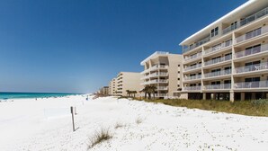 Ein Strandhotel mit mehreren Balkonen, einem Sandstrand und blauem Himmel.