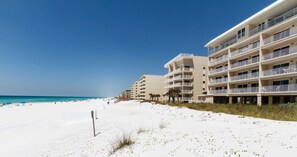 Ein Strandhotel mit mehreren Balkonen, einem Sandstrand und blauem Himmel.