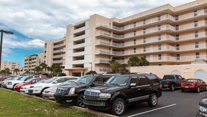 Ein Parkplatz mit mehreren Autos und ein Mehrfamilienhaus mit Balkonen im Hintergrund.