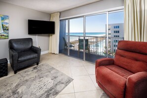 A living room with a large window, a flat-screen TV, a red sofa, a black leather chair, and a gray rug. - Islander 606 - Chill by the Sea (Fort Walton Beach)