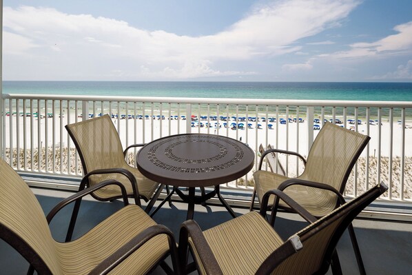 A balcony with a round table and four chairs, overlooking a beach with numerous umbrellas and a clear view of the ocean. - Islander 7008 - Memories by the Sea (Fort Walton Beach)