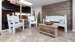 A lobby with white chairs and a wooden bench, an exit sign, and a wooden wall. - Gulf Dunes 504 - Emerald Sea Oasis (Fort Walton Beach)