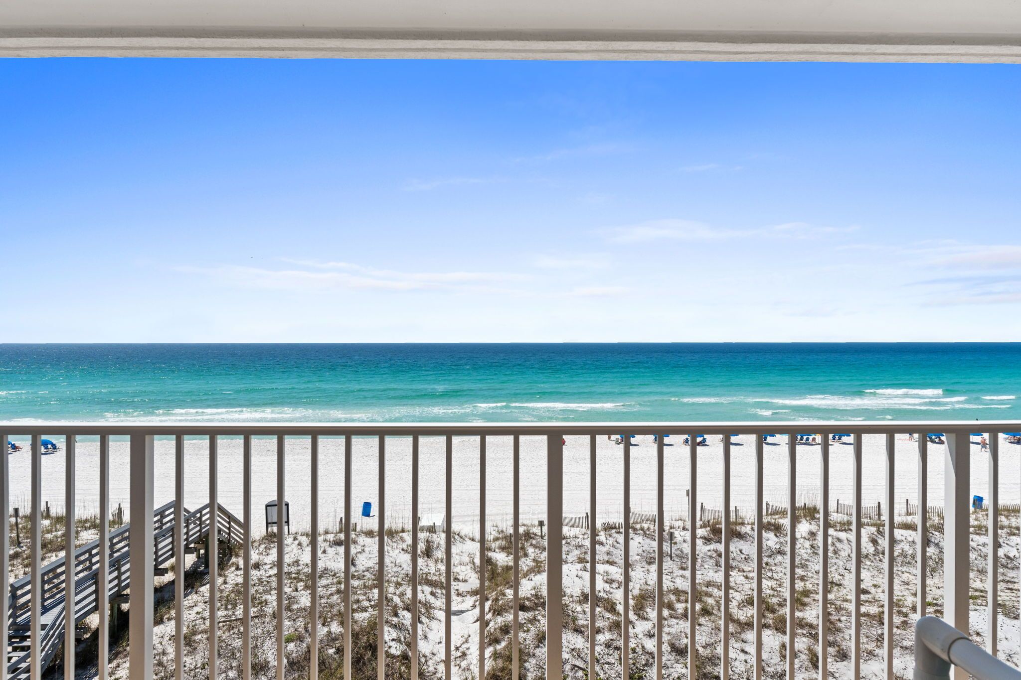 A beach view from a balcony with a railing, sandy beach, and ocean.