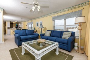 Ein Wohnzimmer mit zwei blauen Sofas, einem Glastisch und einem Deckenventilator.