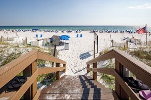 Eine Holztreppe führt zu einem Strand mit Sonnenschirmen und Liegestühlen.