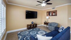 A living room with a blue sofa, a patterned rug, a flat-screen TV, a ceiling fan, and a painting on the wall. - Islander 4006 - Blue Waters and Beyond (Fort Walton Beach)