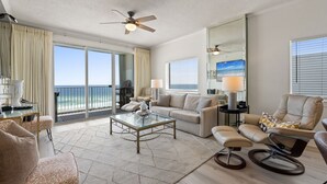 A spacious living room with a glass coffee table, a sofa, and a recliner. There is a balcony with a view of the ocean. - Gulf Dunes 617 - Sand Dollar Daze (Fort Walton Beach)