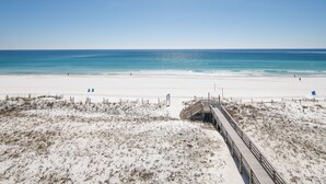 A beach with a wooden boardwalk leading to the water, sandy dunes, and a clear blue sky.