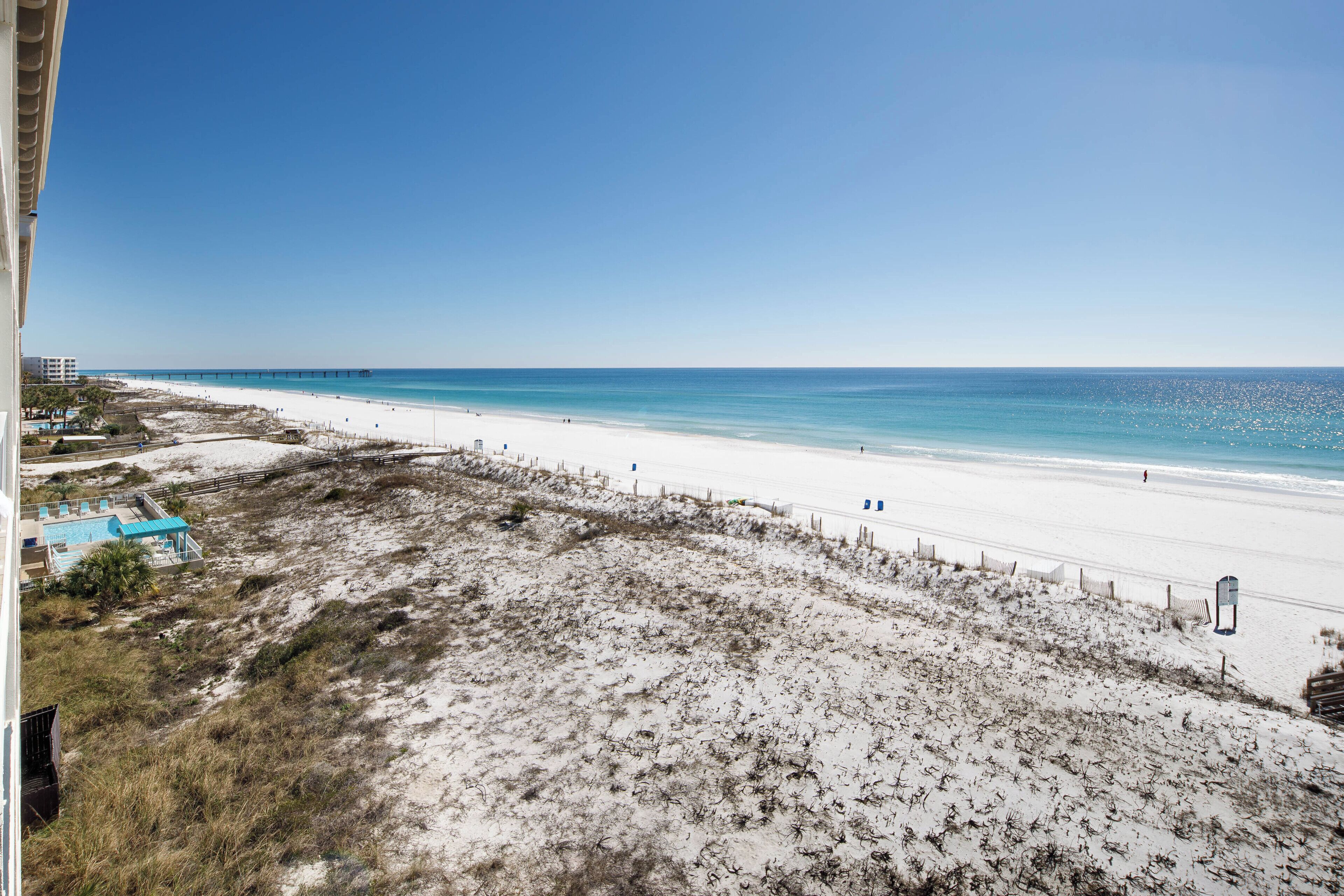 A beach with a long pier extending into the ocean, a sandy beach, and a few buildings in the background.