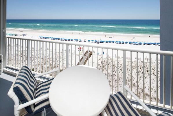 Een balkon met uitzicht op een strand, een witte balustrade en gestreepte kussens.