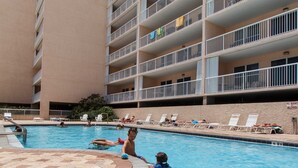 Una piscina con borde de baldosas, rodeada por un edificio de varios pisos con balcones.