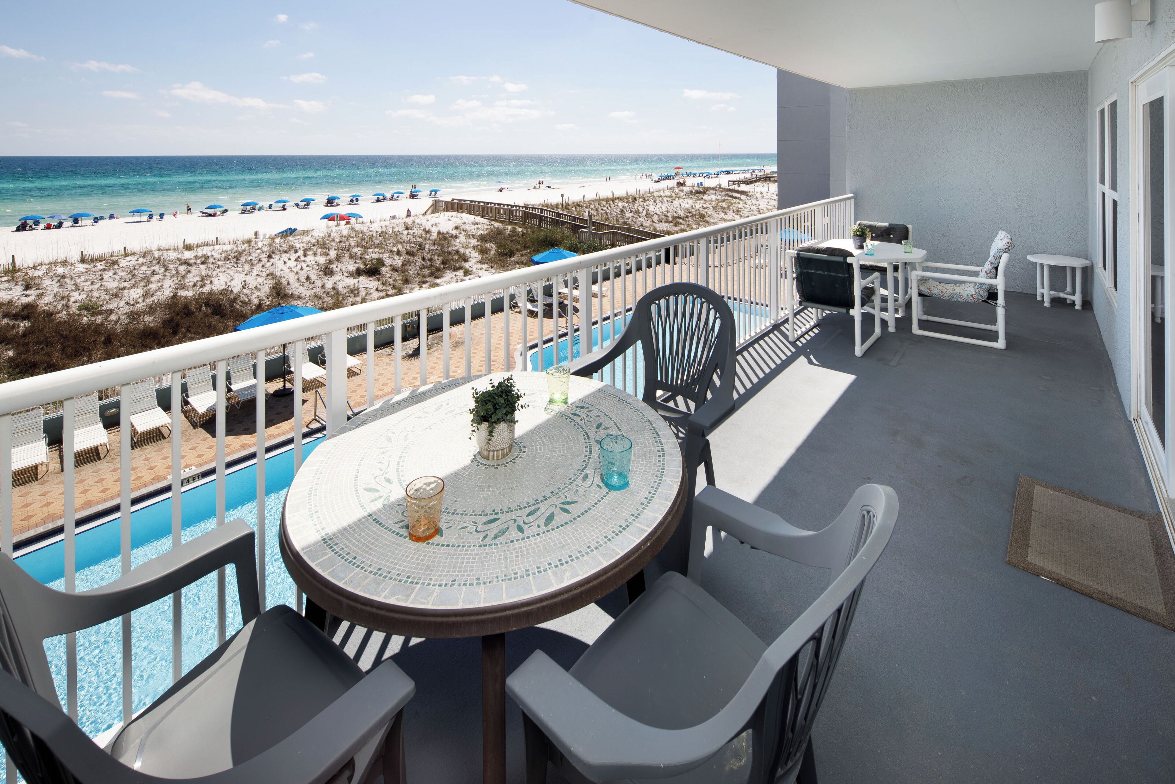 Un balcon avec vue sur la plage, une piscine et une table avec des chaises.