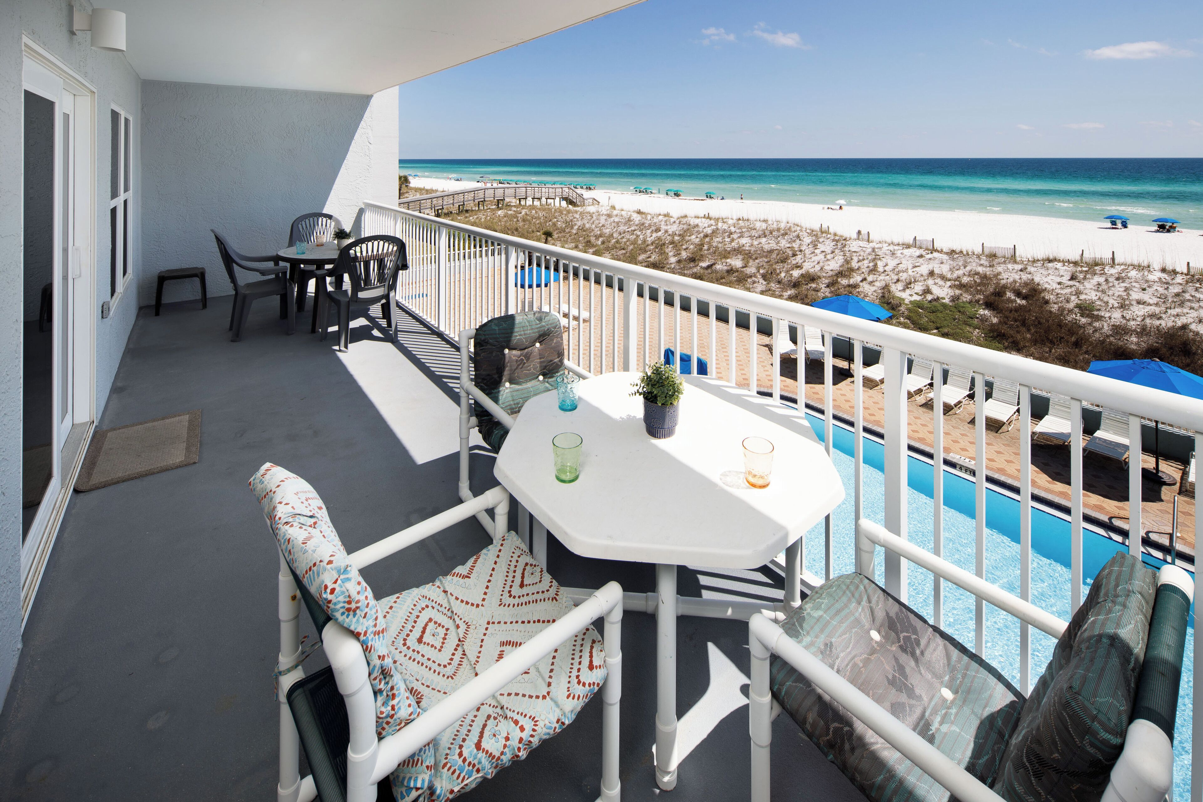 Un balcone con tavolo e sedie, una piscina e vista sulla spiaggia.