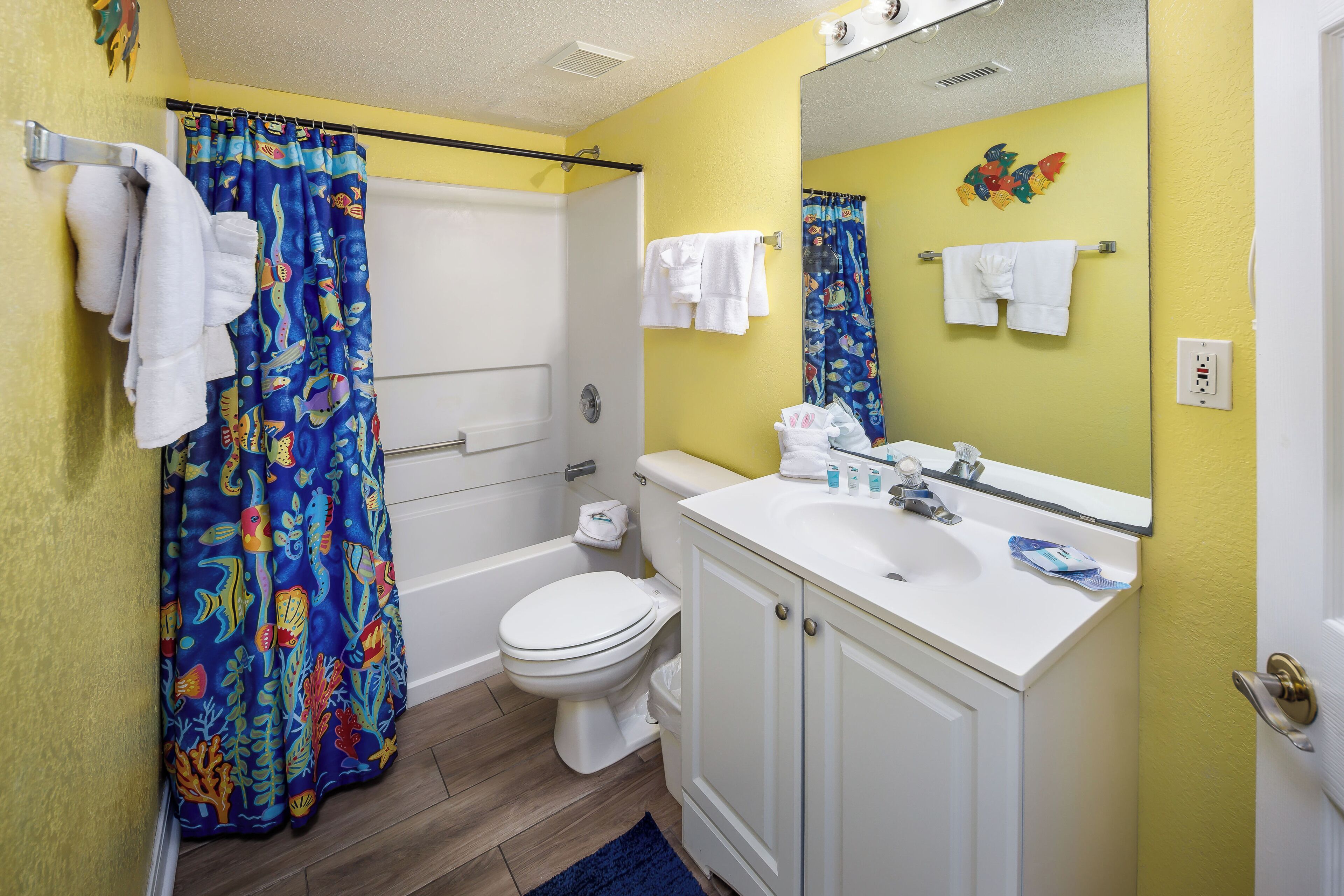 A bathroom with a shower curtain, a toilet, a sink, and a mirror.