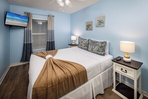A bedroom with a bed, a nightstand, a TV, and a window with curtains. - Islander 3006 - Sandy Smiles (Fort Walton Beach)