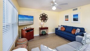 Ein Wohnzimmer mit Sofa, Hocker und Fernseher auf einem Schrank.