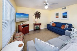 A living room with a sofa, ottoman, and a television on a stand. - Islander 3006 - Sandy Smiles (Fort Walton Beach)