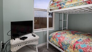 Un letto a castello con copriletto floreale colorato, una televisione su una scrivania in vimini e una finestra con vista all'esterno.