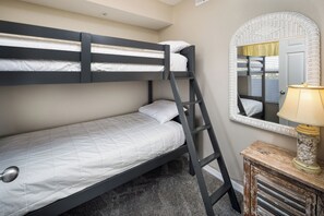 Una cama litera con escalera, una mesita de noche con lámpara y un espejo con marco de mimbre.