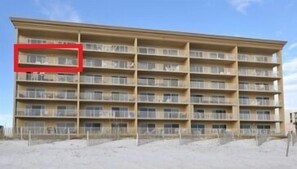 Ein mehrgeschossiges Hotel mit Balkonen, einem sandigen Erdgeschoss und blauem Himmel.