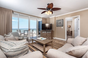 A spacious living room with a large television, a ceiling fan, and a view of the ocean through the sliding glass doors. - Island Princess 309 - Splash of Paradise (Fort Walton Beach)