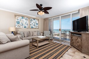 A living room with a sofa, coffee table, and a TV on a wooden cabinet. There are two large windows with a view of the ocean. - Island Princess 309 - Splash of Paradise (Fort Walton Beach)