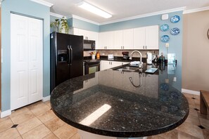 A kitchen with white cabinets, a black refrigerator, a microwave, a sink, and a granite countertop. - Island Princess 309 - Splash of Paradise (Fort Walton Beach)