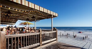 A beachside restaurant with outdoor seating, a wooden deck, and a view of the ocean. - Islander 6004 by Brooks and Shorey Resorts (Fort Walton Beach)
