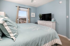 A bedroom with a bed, a television on a dresser, a window with curtains, and a view of the outside. - Islander 6004 by Brooks and Shorey Resorts (Fort Walton Beach)