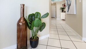 En gang med en potteplante og en vase, klinkegulv og et billede på væggen.