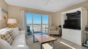 Una sala de estar con sofá, mesa de centro, televisor y balcón con vista a la playa.