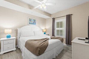 A hotel room with a bed, nightstands, a ceiling fan, a window with curtains, and a painting on the wall. - Gulf Dunes 505 - Tide Turner (Fort Walton Beach)