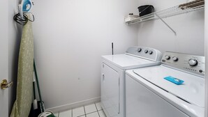 Une buanderie équipée d’un lave-linge et d’un sèche-linge, d’un balai et d’un étendoir pour le linge, ainsi que de produits de nettoyage.