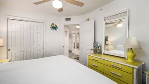 Une chambre à coucher avec un lit, une commode jaune, un miroir et un ventilateur de plafond.